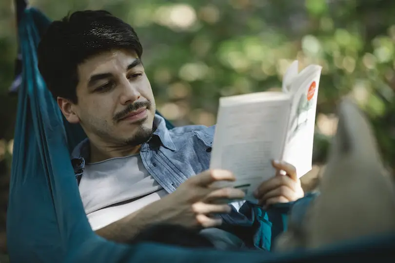 Focused bearded man with book on hammock