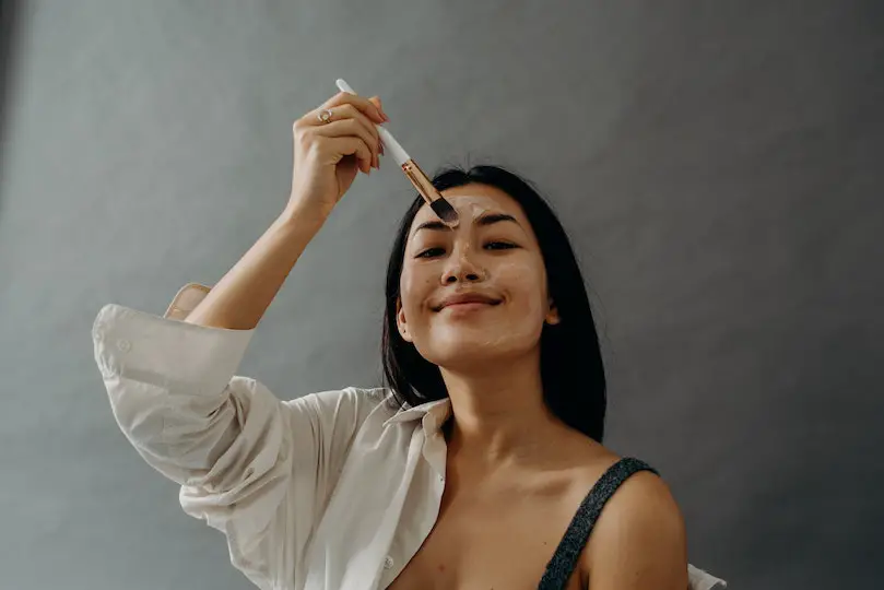 A Woman Applying a Cream on Her Face Using a Makeup Brush