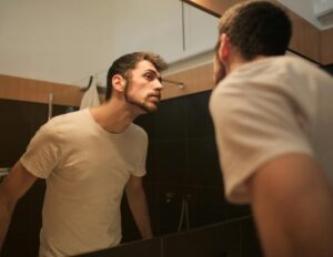 Stylish concentrated man looking in mirror in bathroom