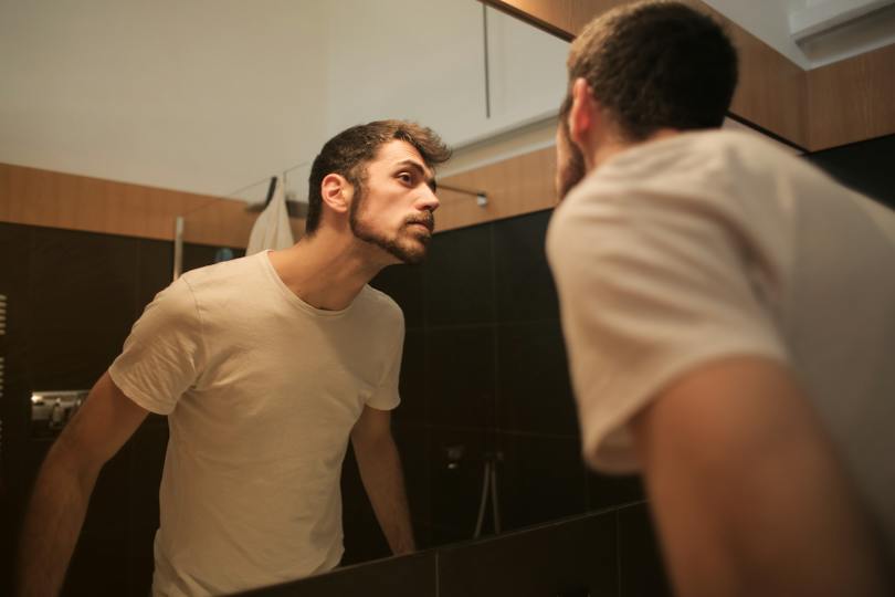Stylish concentrated man looking in mirror in bathroom